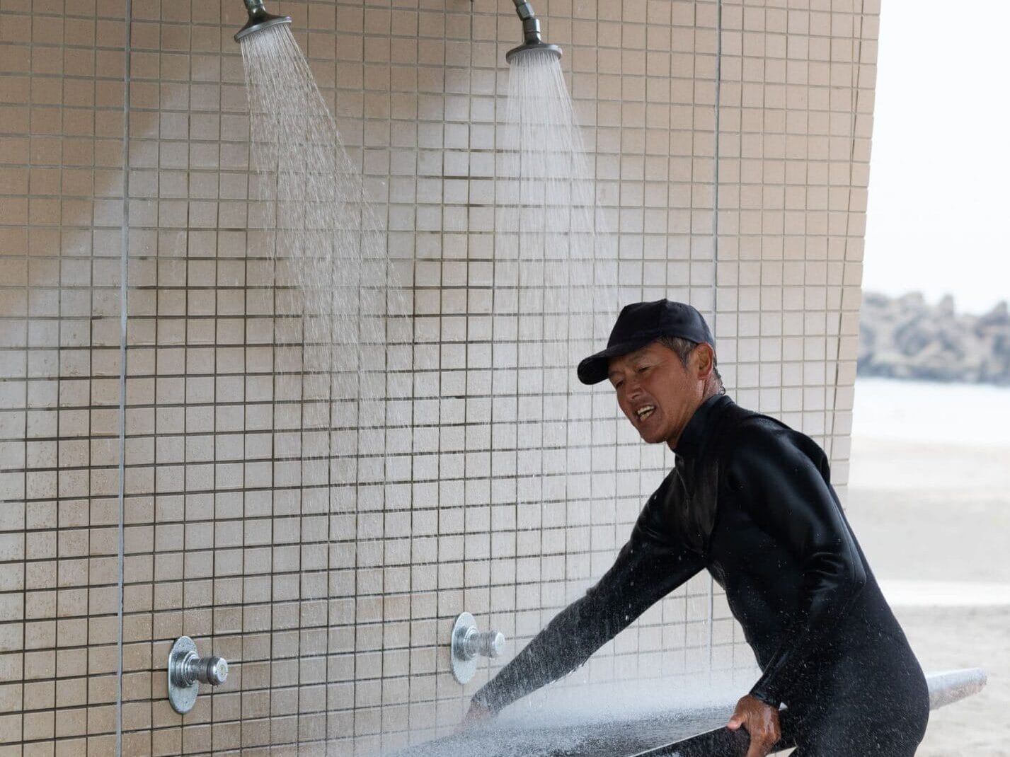Man spült sein Surfbrett unter der Dusche nach dem Surfen
