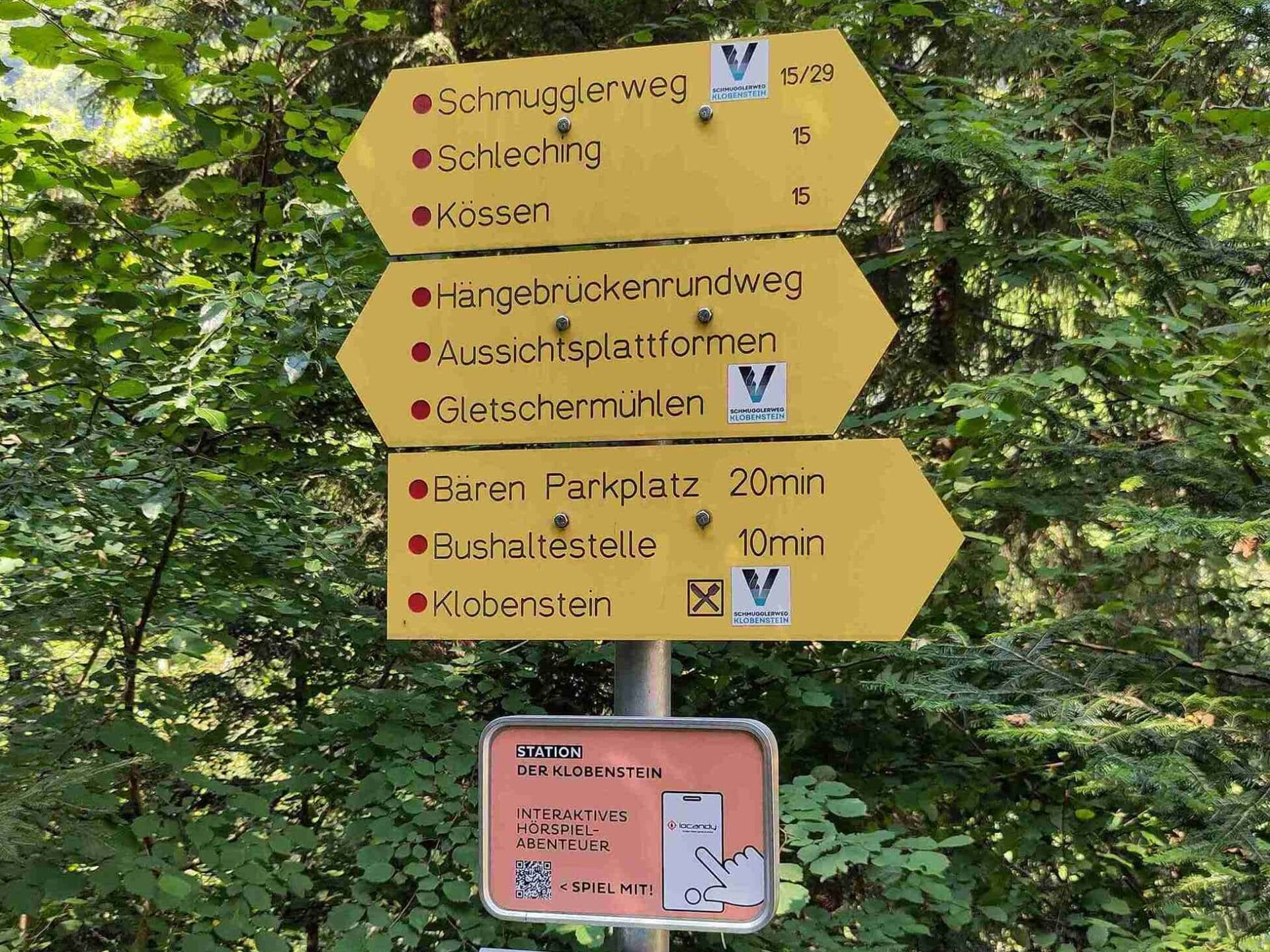 Ein Wegweiser mit Stempel für Rätselwanderung und Schild mit einem QR Code für ein interaktives Hörspiel-Abenteuer