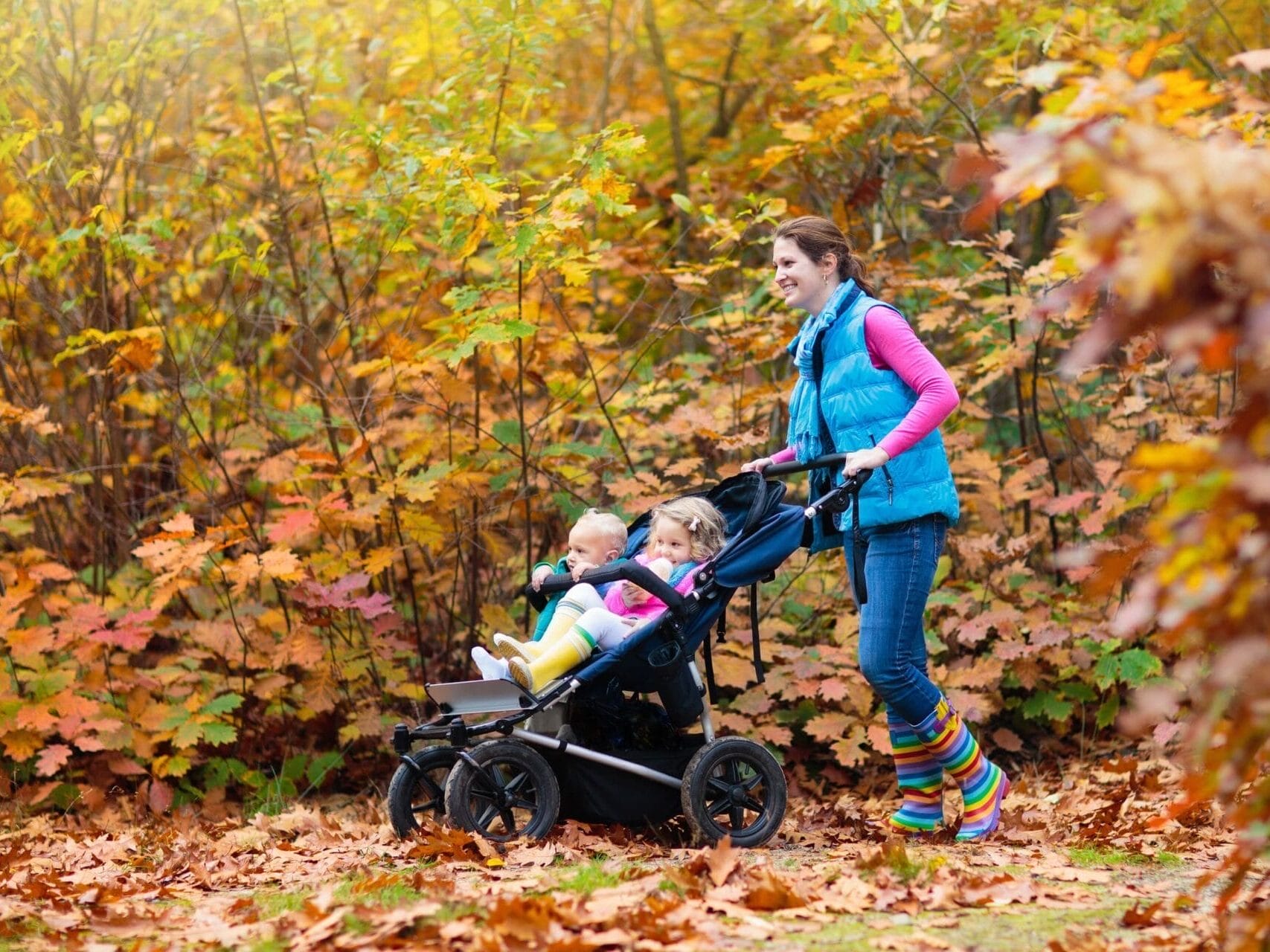 Frau schiebt ihre Kinder mit dem Kinderwagen durch den Wald.