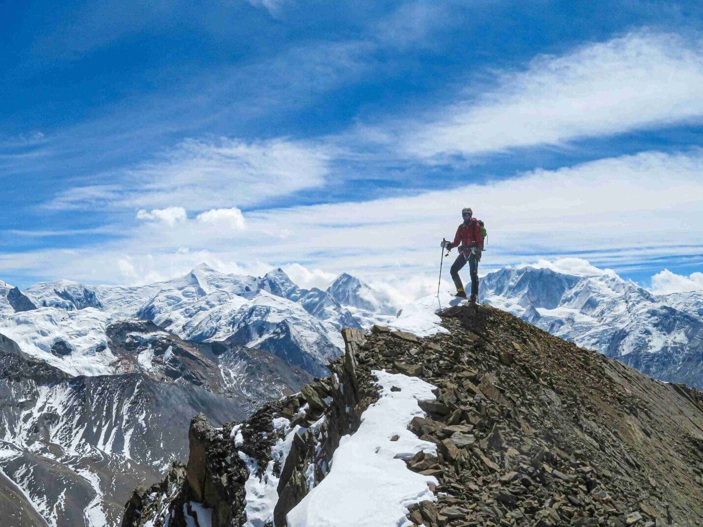 Eine Person oben am Gipfel mit schneebedeckten Bergen im Hintergrund