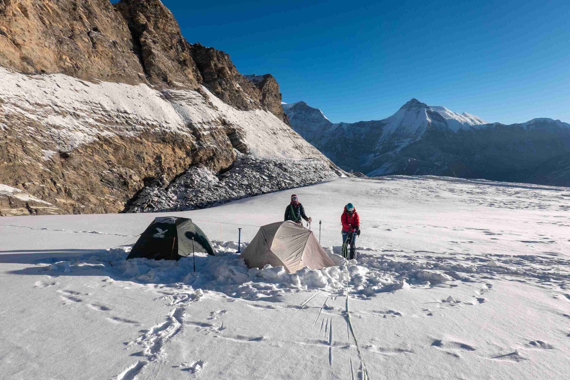Zwei Zelte mitten im Schnee mit Felswänden und Bergen im Hintergrund