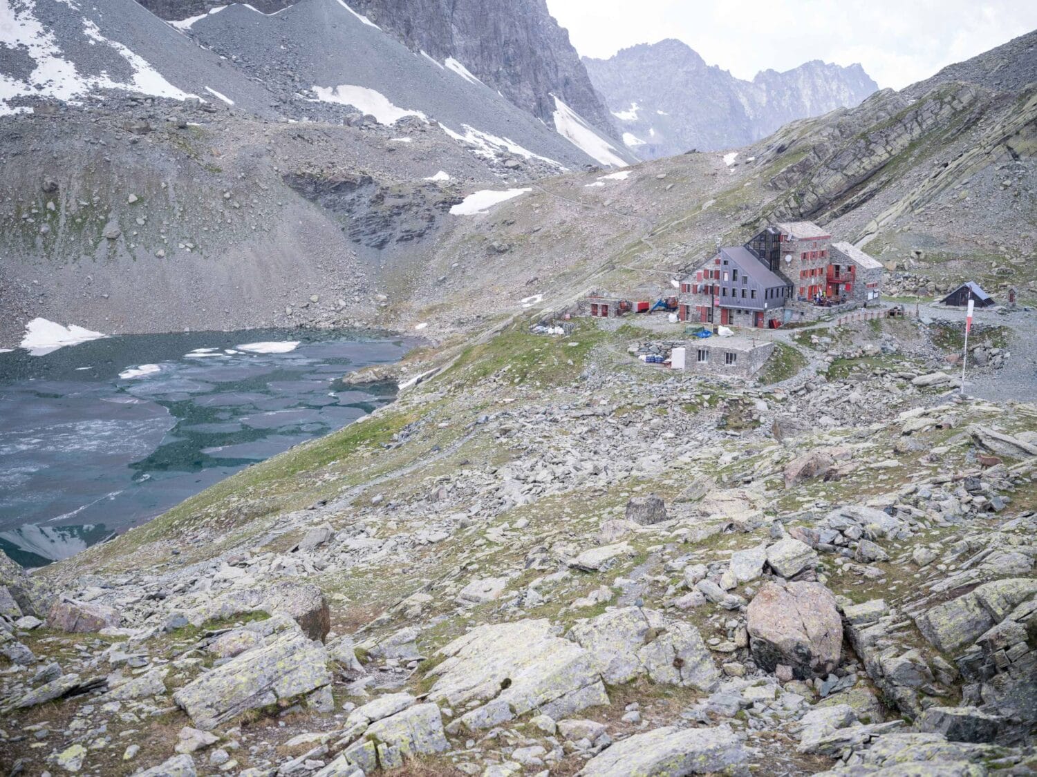 Das Rifugio Quintino Sella mit dem teilweise eisbedeckten Lago Grande di Viso.