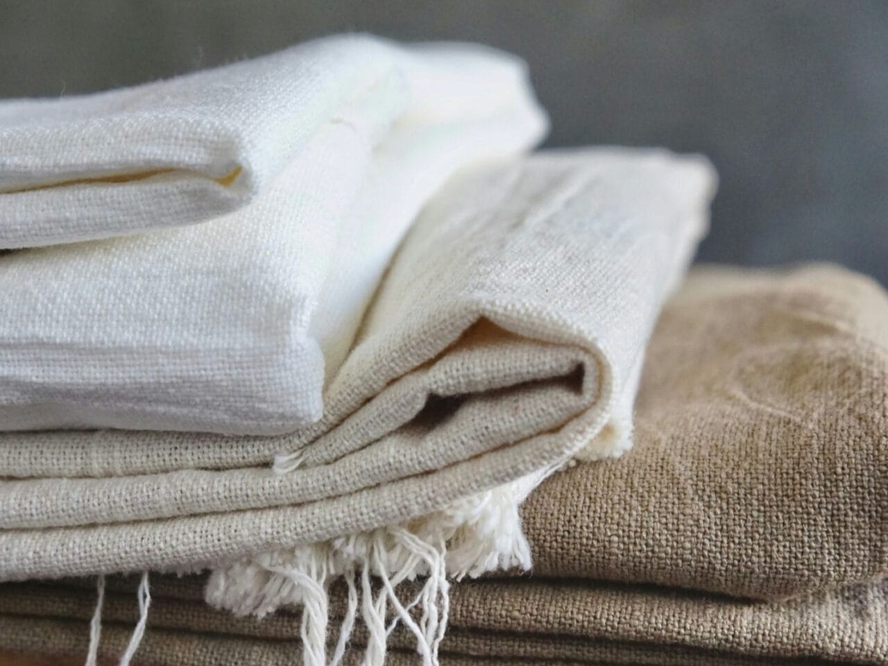 Gefaltete Leinenstoffe in Weiß, Beige und Braun auf einem Holztisch