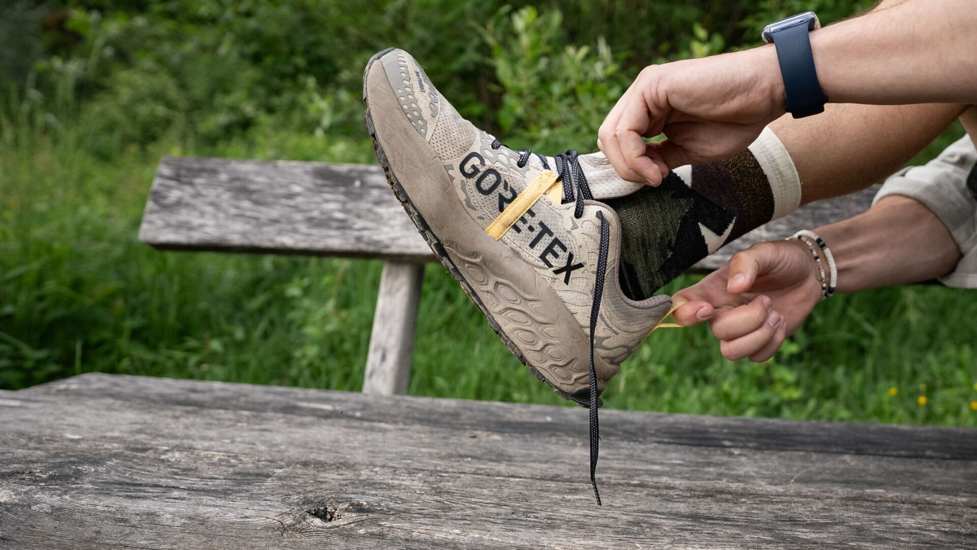 Jemand zieht sich seinen linken Schuh über einer Bank in der Natur an.