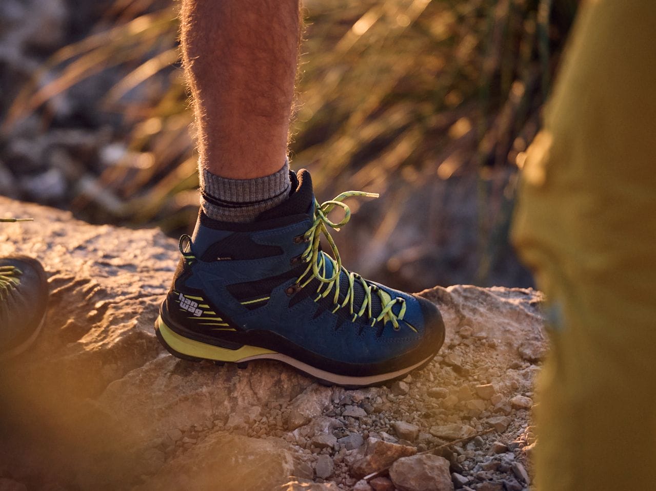 Close-Up von einem blauen Wanderschuh auf einem Fels stehend.