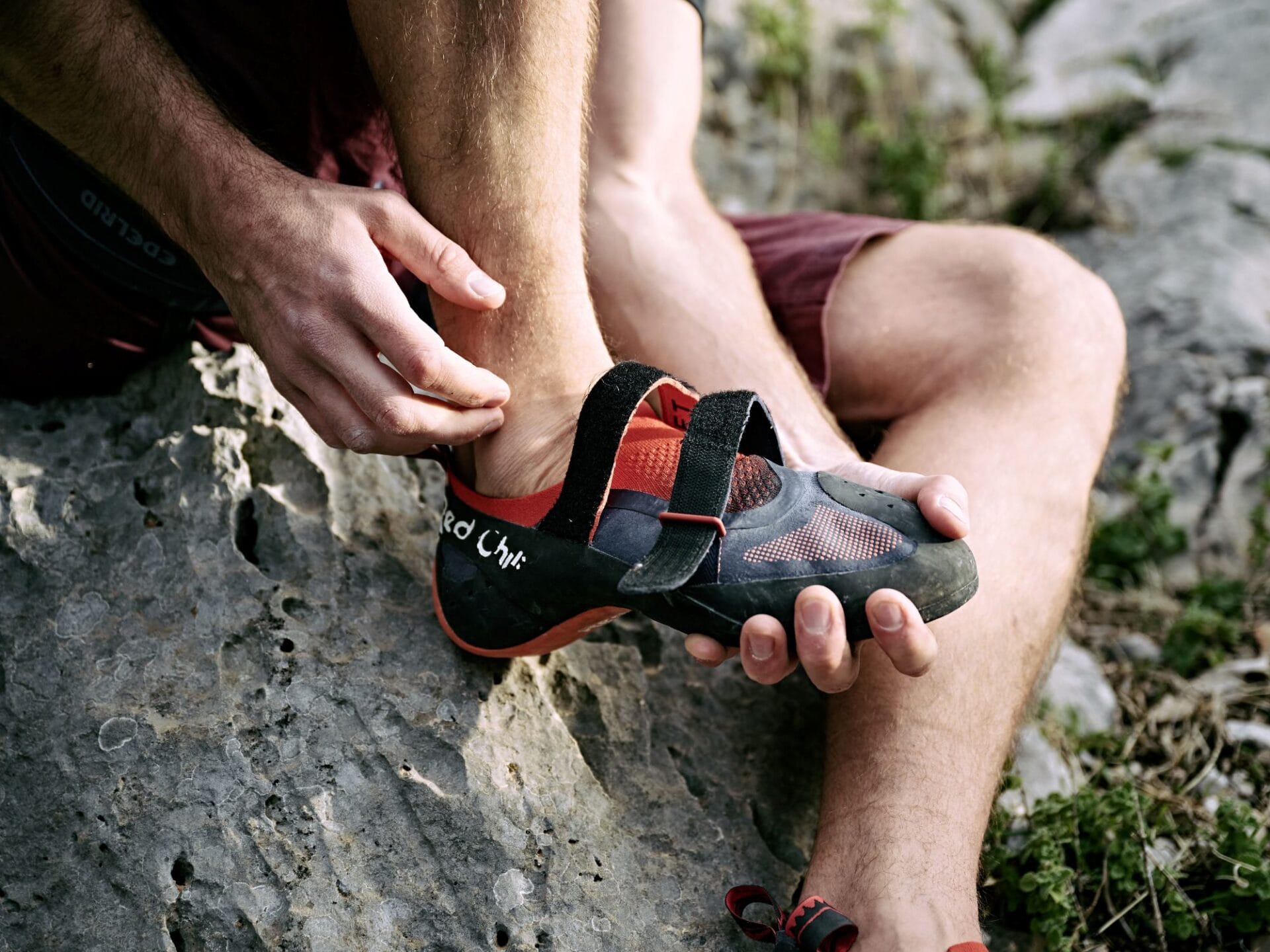 Kletterer sitzt auf einem Fels und zieht sich seinen rechten Kletterschuh aus.