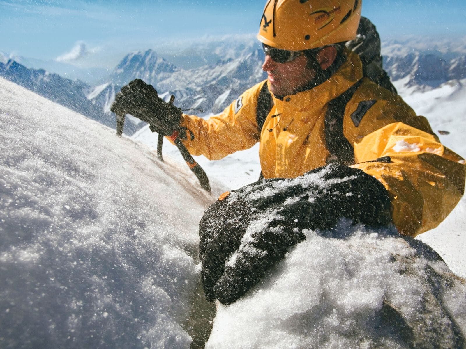 Mann im Schnee mit Gore-Tex Handschuhen und gelber Jacke und Helm