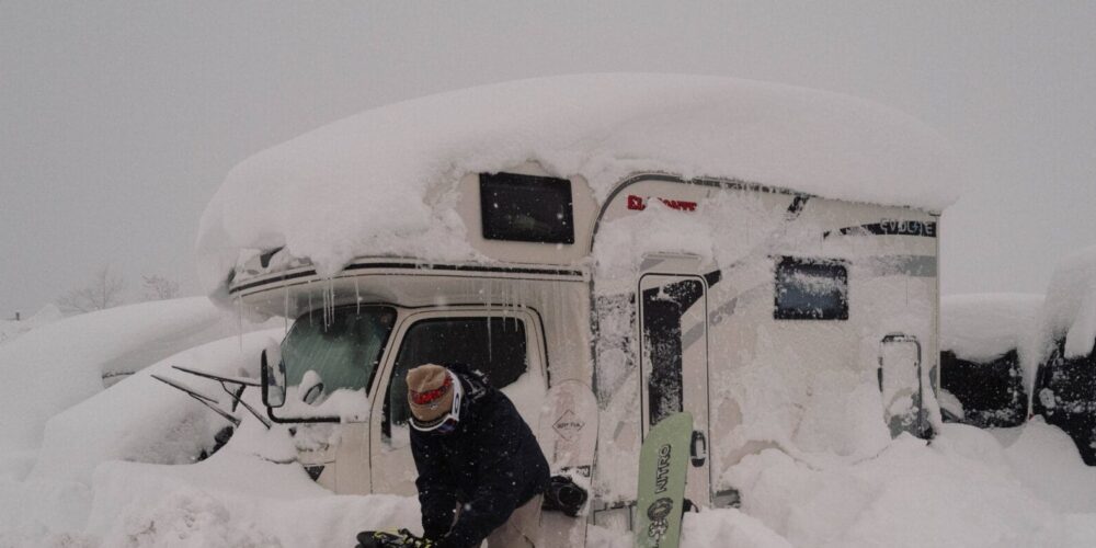 Eingeschneiter Camper und Snowboarder davor